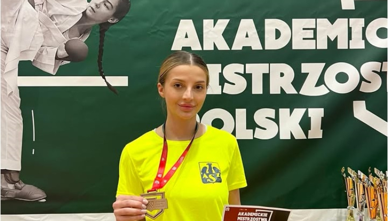 kobieta w żółtym podkoszulku prezentuje dyplom i brązowy medal za udział w zawodach
