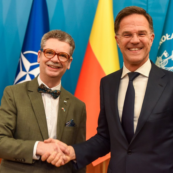 dwoje mężczyzn podaj sobie ręce; w tle flagi UE, NATO, Warszawy i SGH